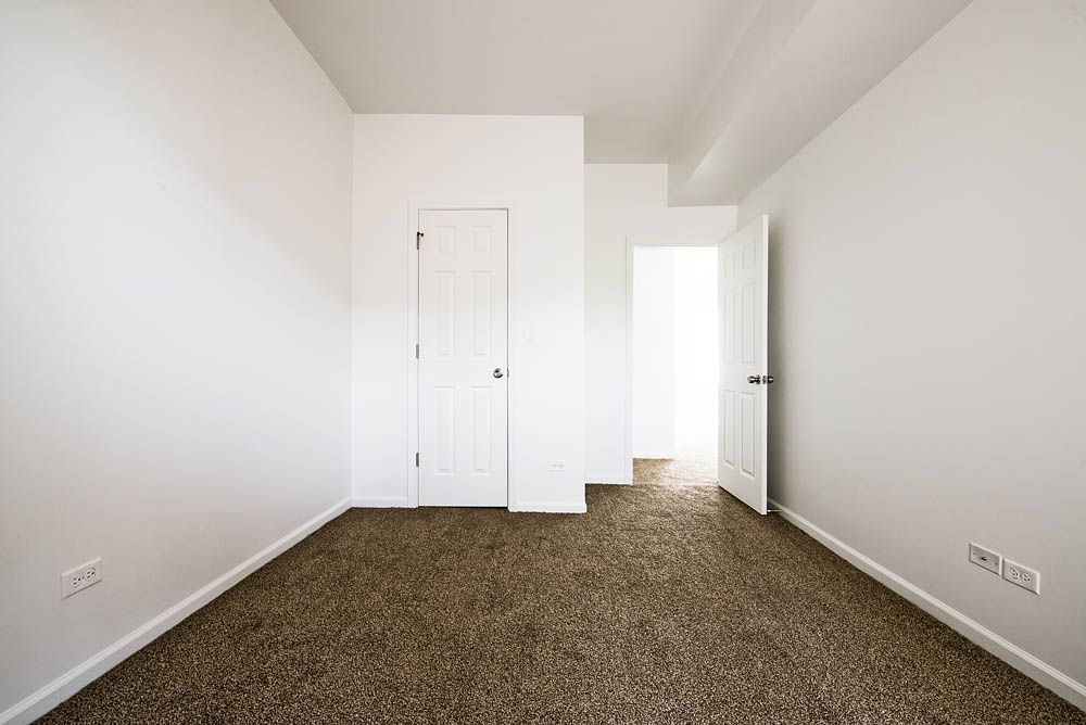 Empty room with white walls, brown carpet, and two white doors.