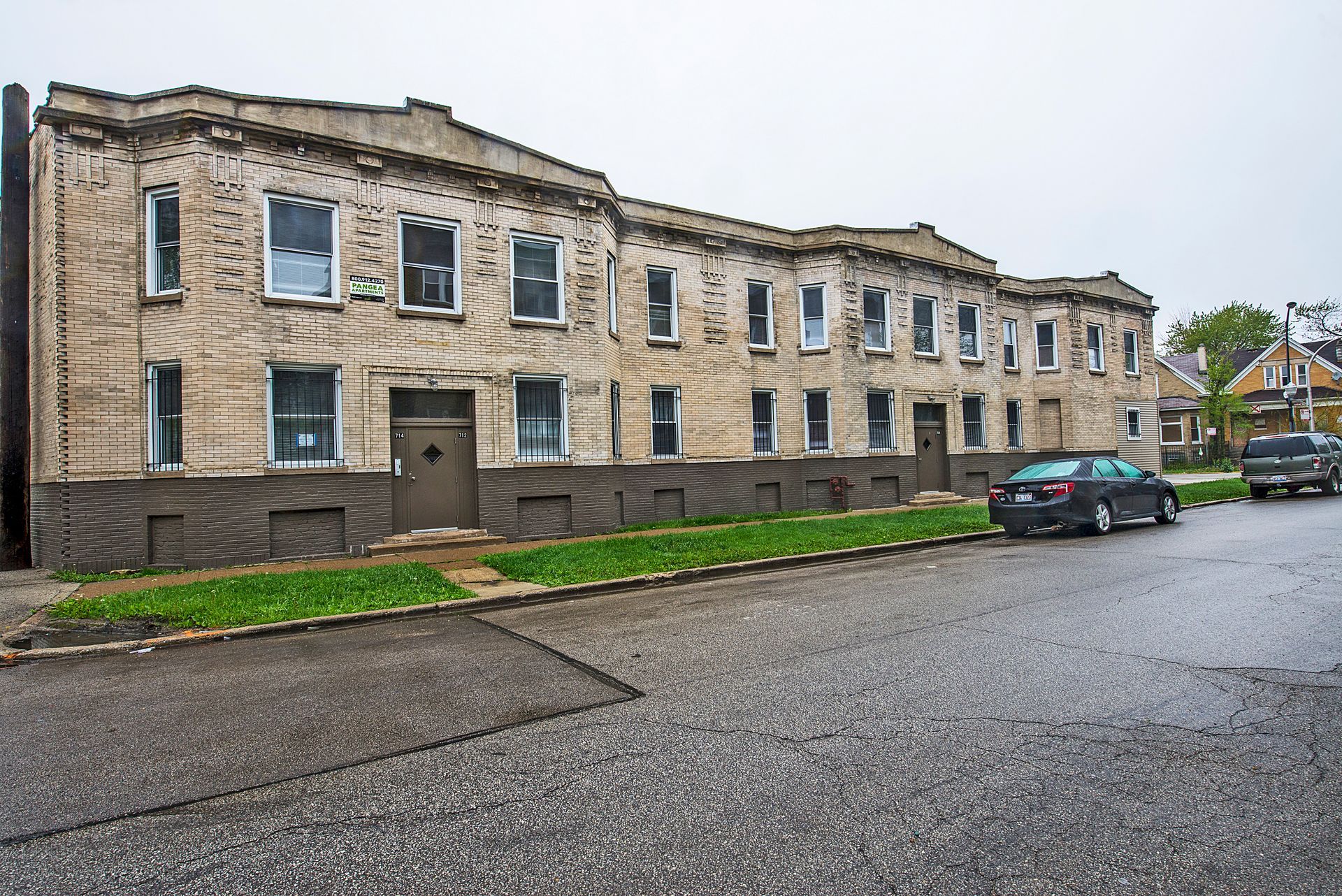 Multi-unit brick building with several windows and doors on a wet street.