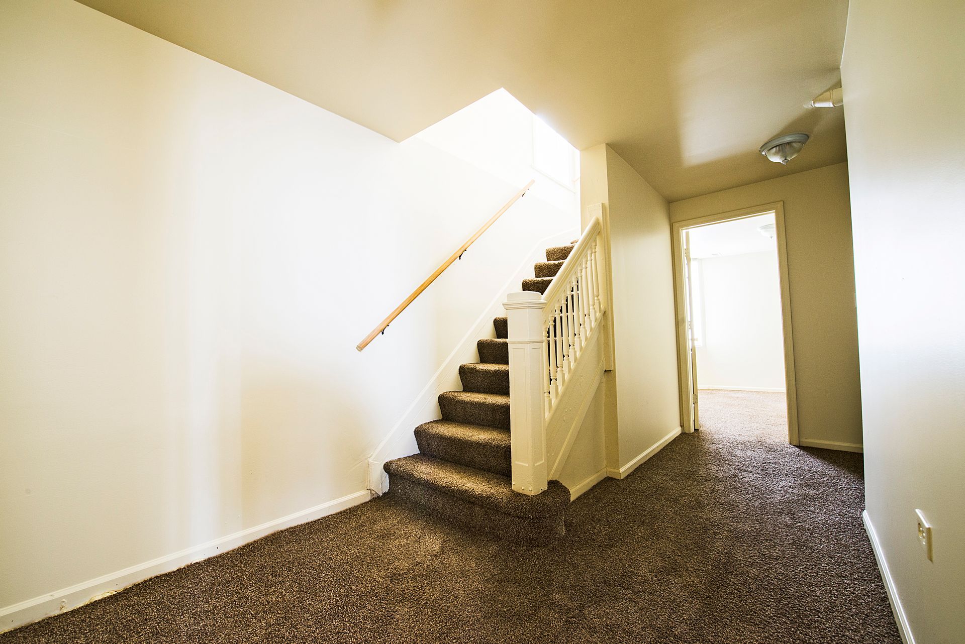 Staircase with brown carpet and wooden handrail; a doorway to another room is on the right.