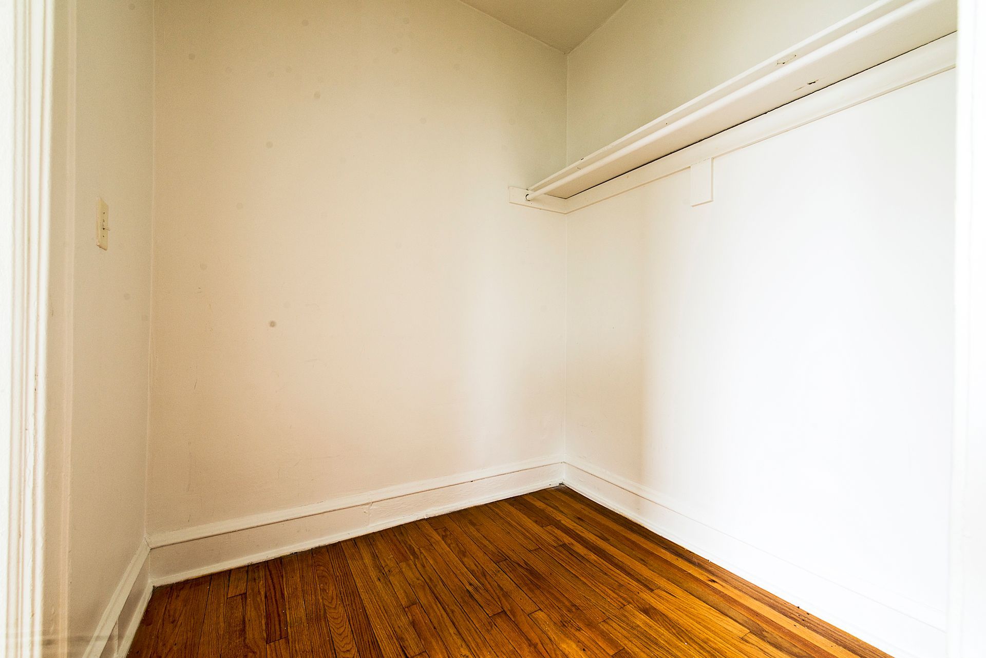 Empty closet with hardwood floor, white walls, and a shelf.