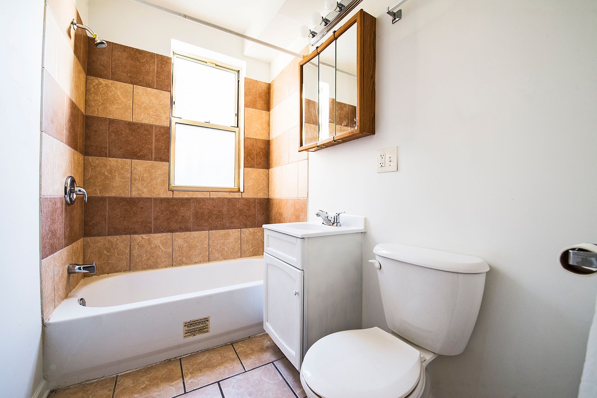 Bathroom with tiled wall above bathtub, window, sink, toilet, and medicine cabinet.