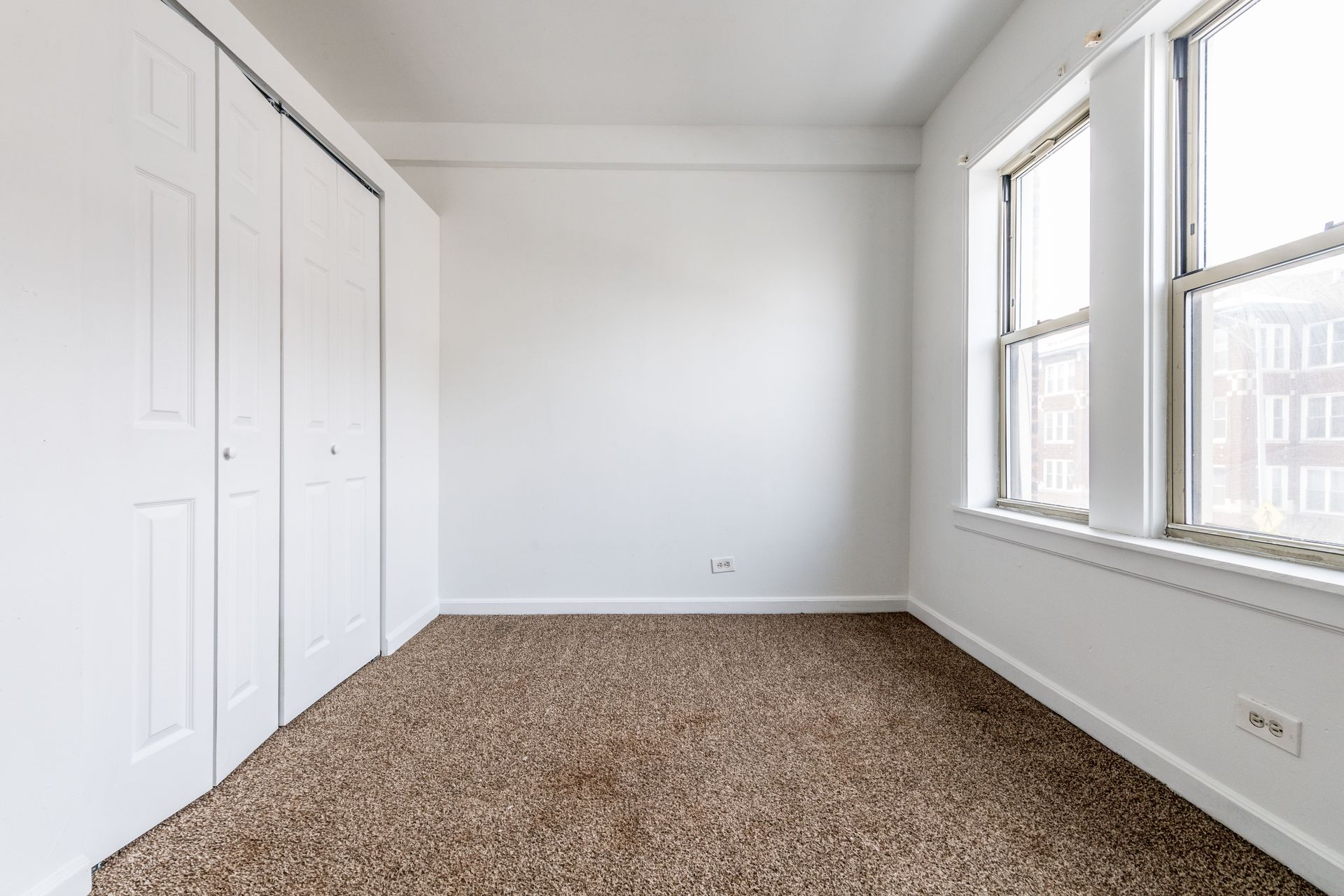 Empty room with white walls, closet, and windows, brown carpet.