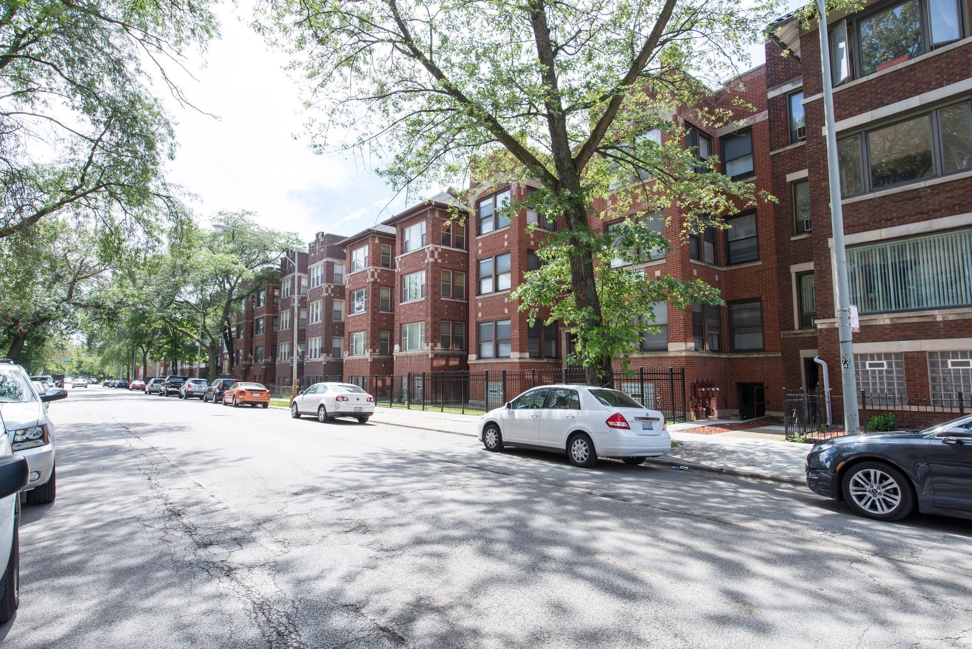 Street view of brick apartment buildings with parked cars and trees.