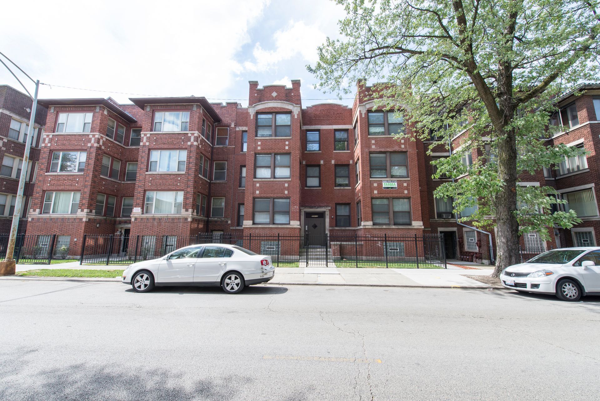 Multi-story red brick apartment building with cars parked on street.