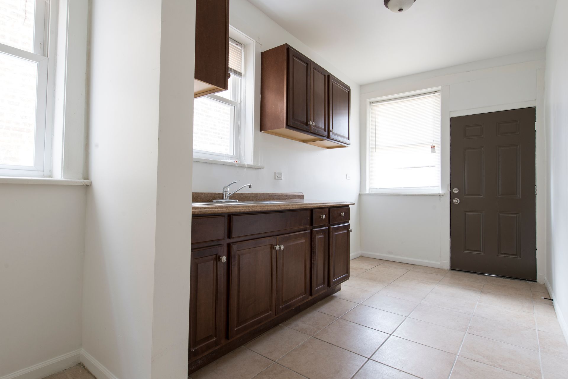 Empty kitchen with brown cabinets, sink, and two windows.