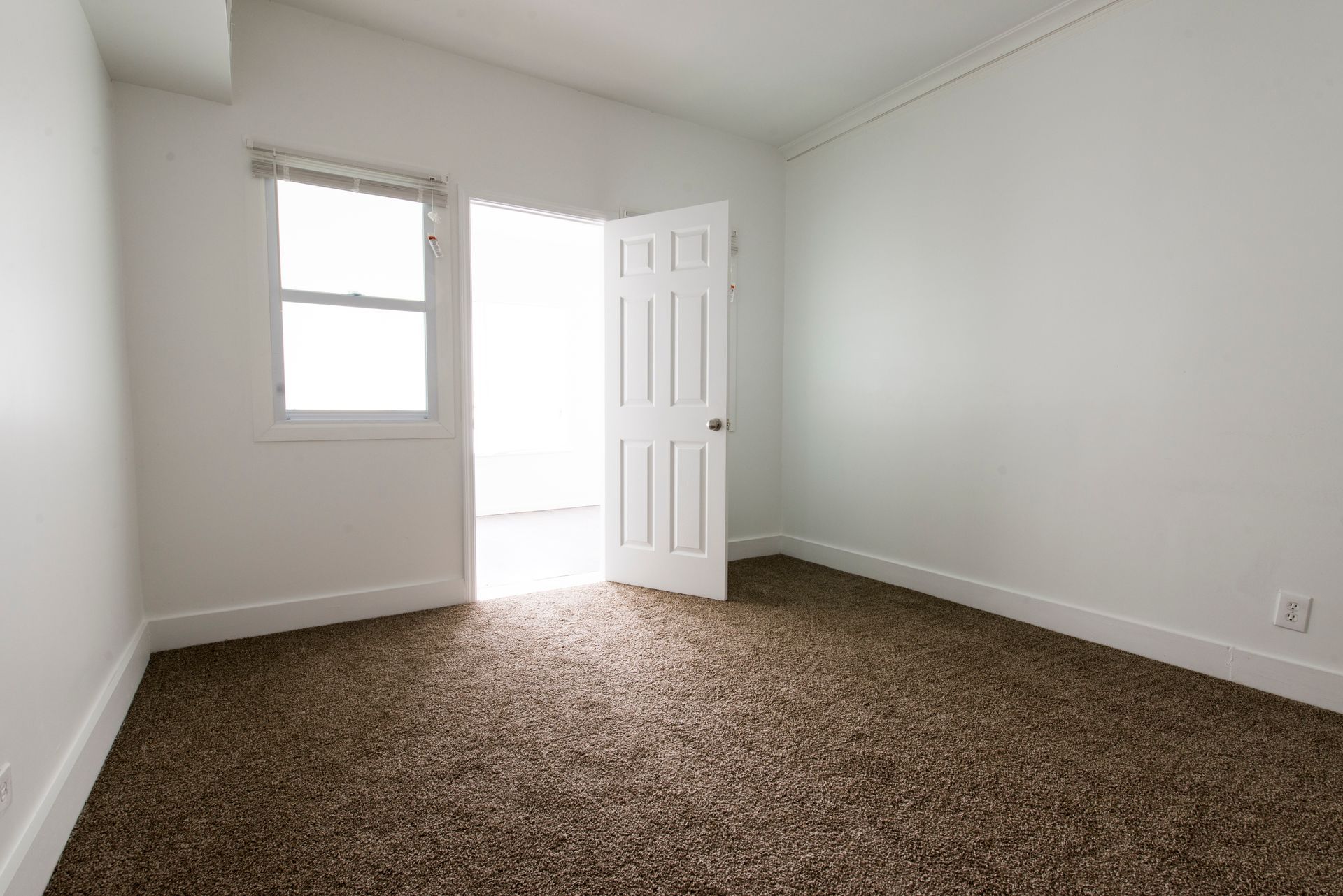 Empty room with brown carpet, white walls, and an open door.