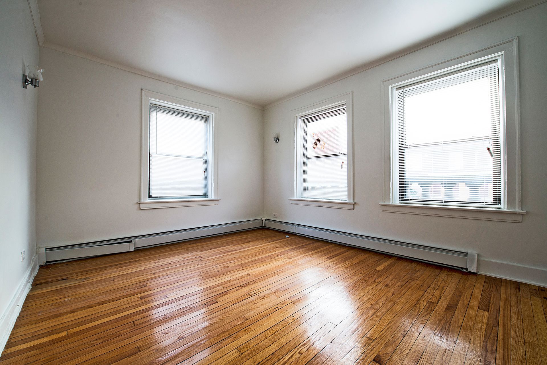 Empty room with hardwood floors, three windows, and white walls.