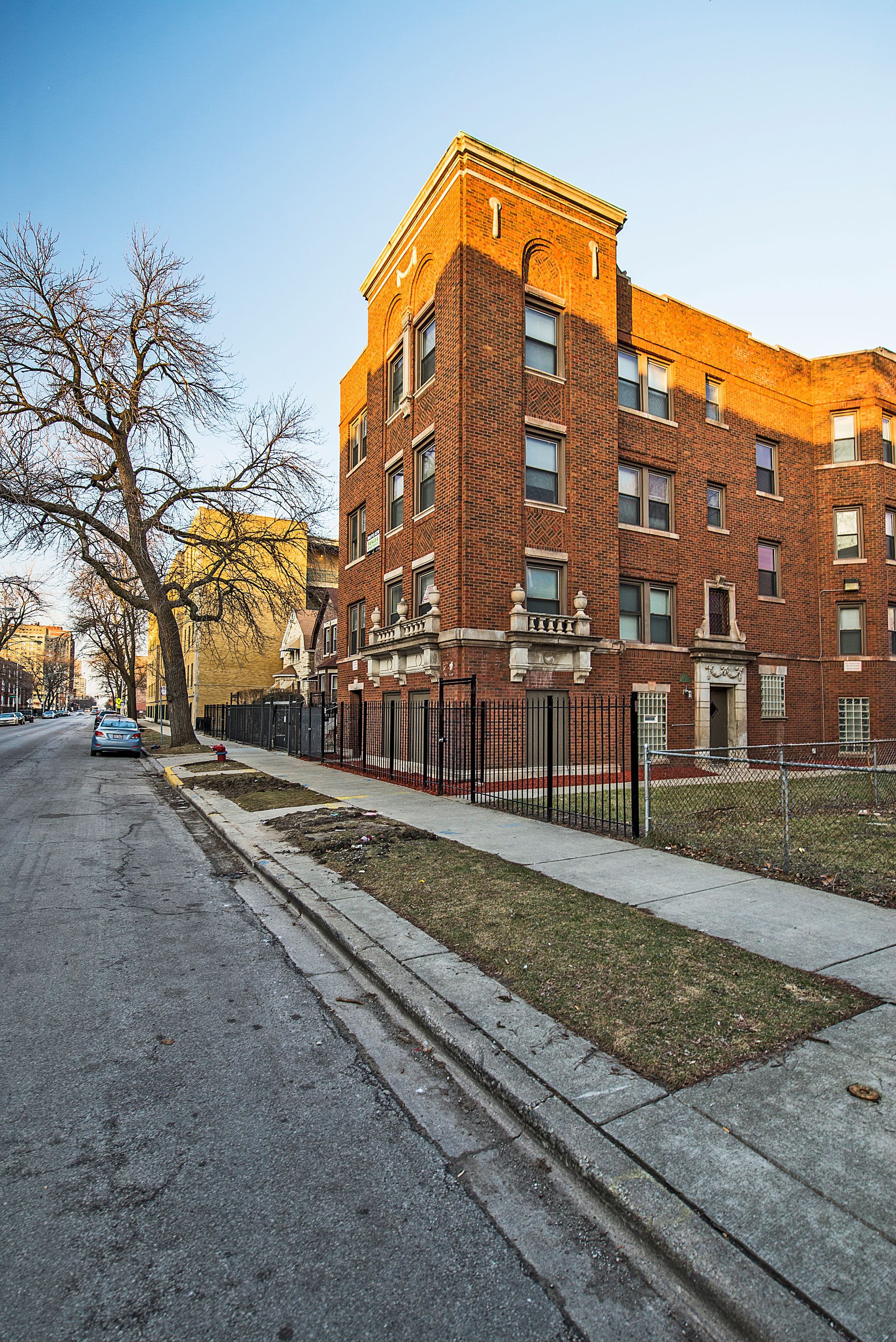 Red brick apartment building on a city street; a tree and blue sky are visible.