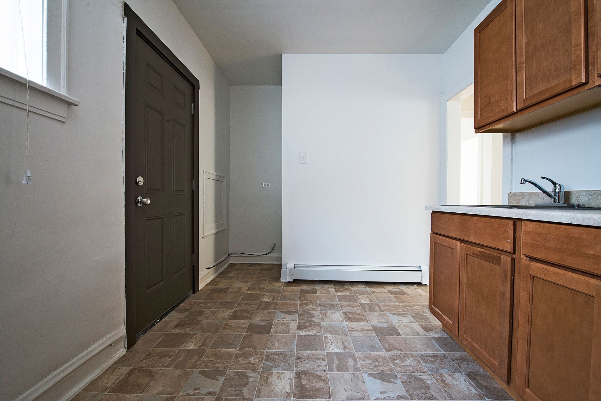 Small kitchen with brown cabinets and a door, neutral colors, and patterned flooring.