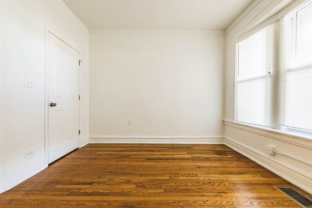 Empty room with wood floor, white walls, door, and window.