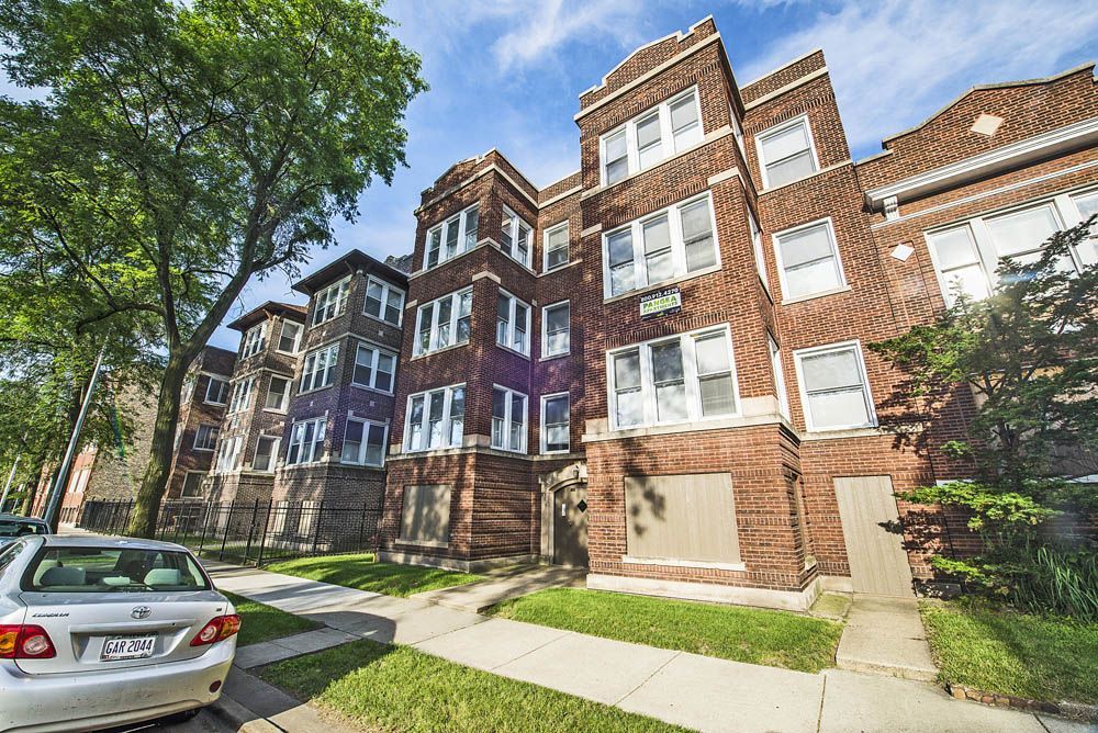 Brick apartment buildings on a city street, car parked in front, sunny day.