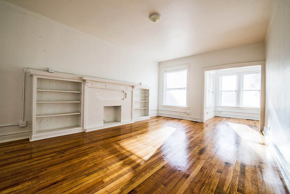 Empty living room with wood floors, built-in shelves, and windows.