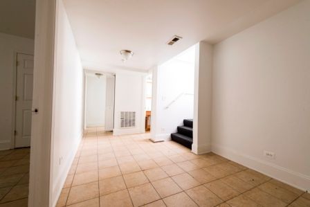 Empty room with tiled floor, white walls, and stairs leading up.