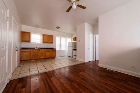 Empty kitchen and living area with wood floors, brown cabinets, and white appliances.