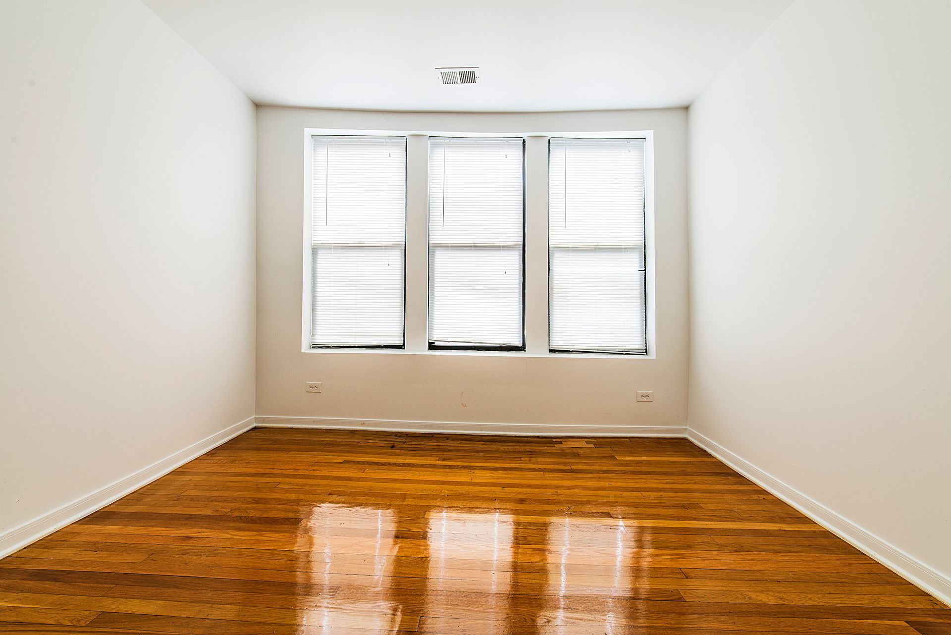 Empty room with hardwood floors, white walls, and a window with blinds.