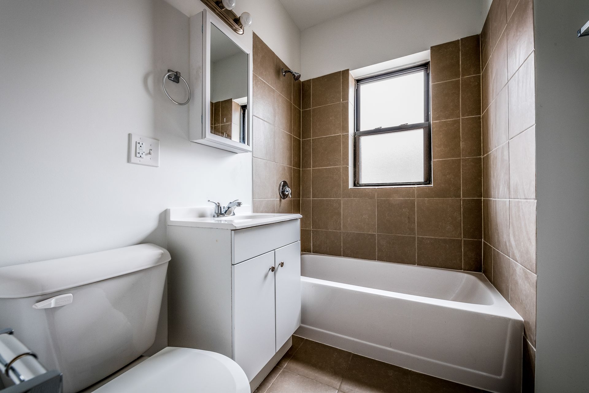 Bathroom with white toilet and vanity, brown tile surround tub, and small window.
