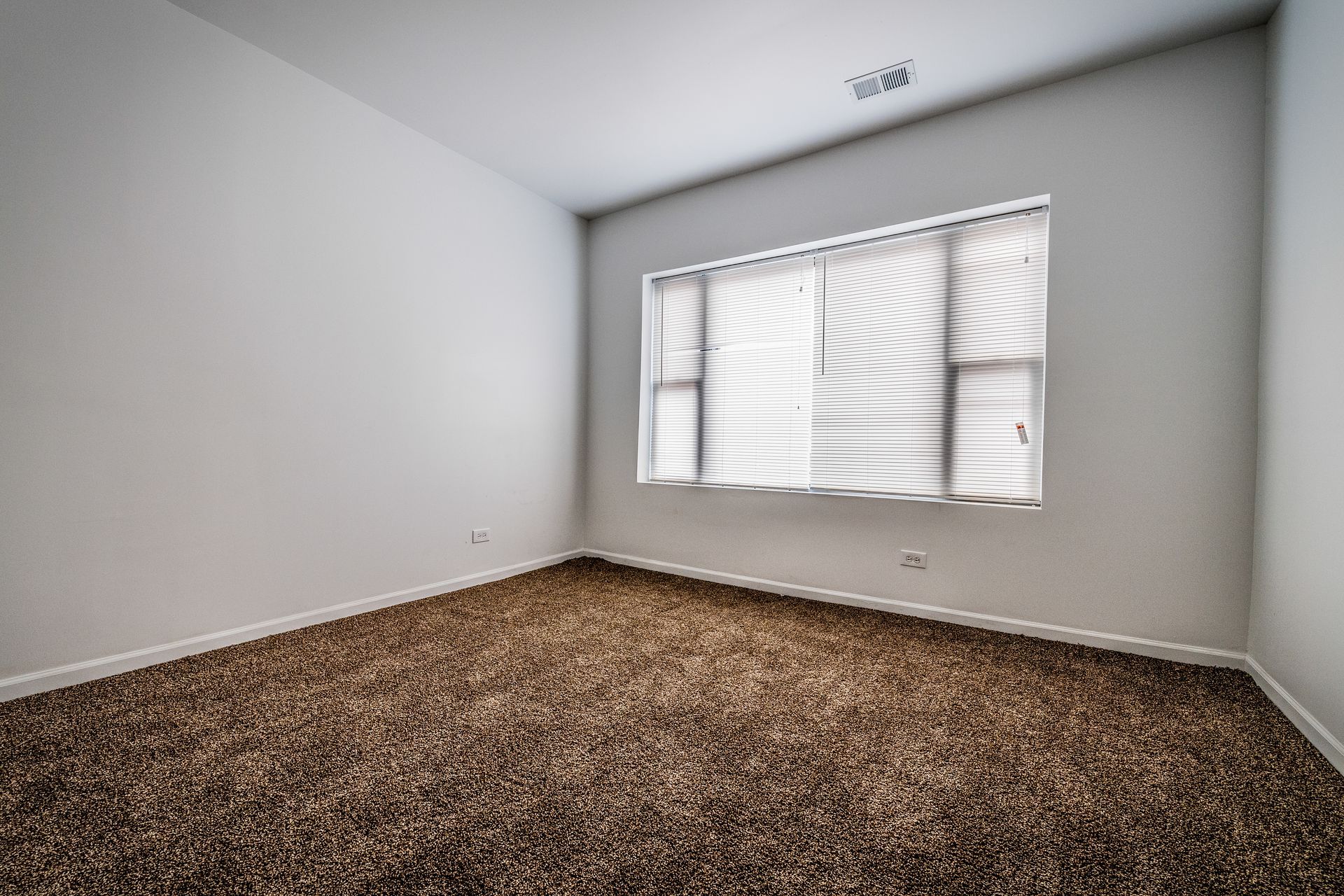 Empty room with brown carpet, white walls, and a window with blinds.