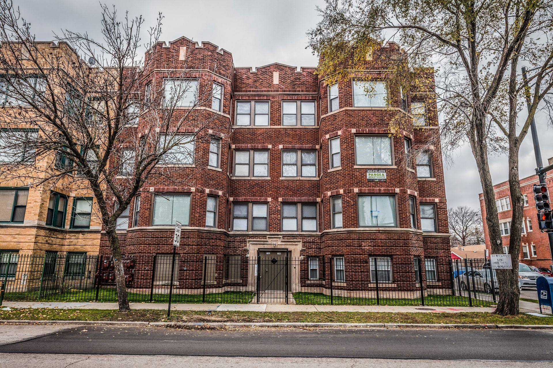 Multi-story brick apartment building with decorative turrets and wrought iron fence.