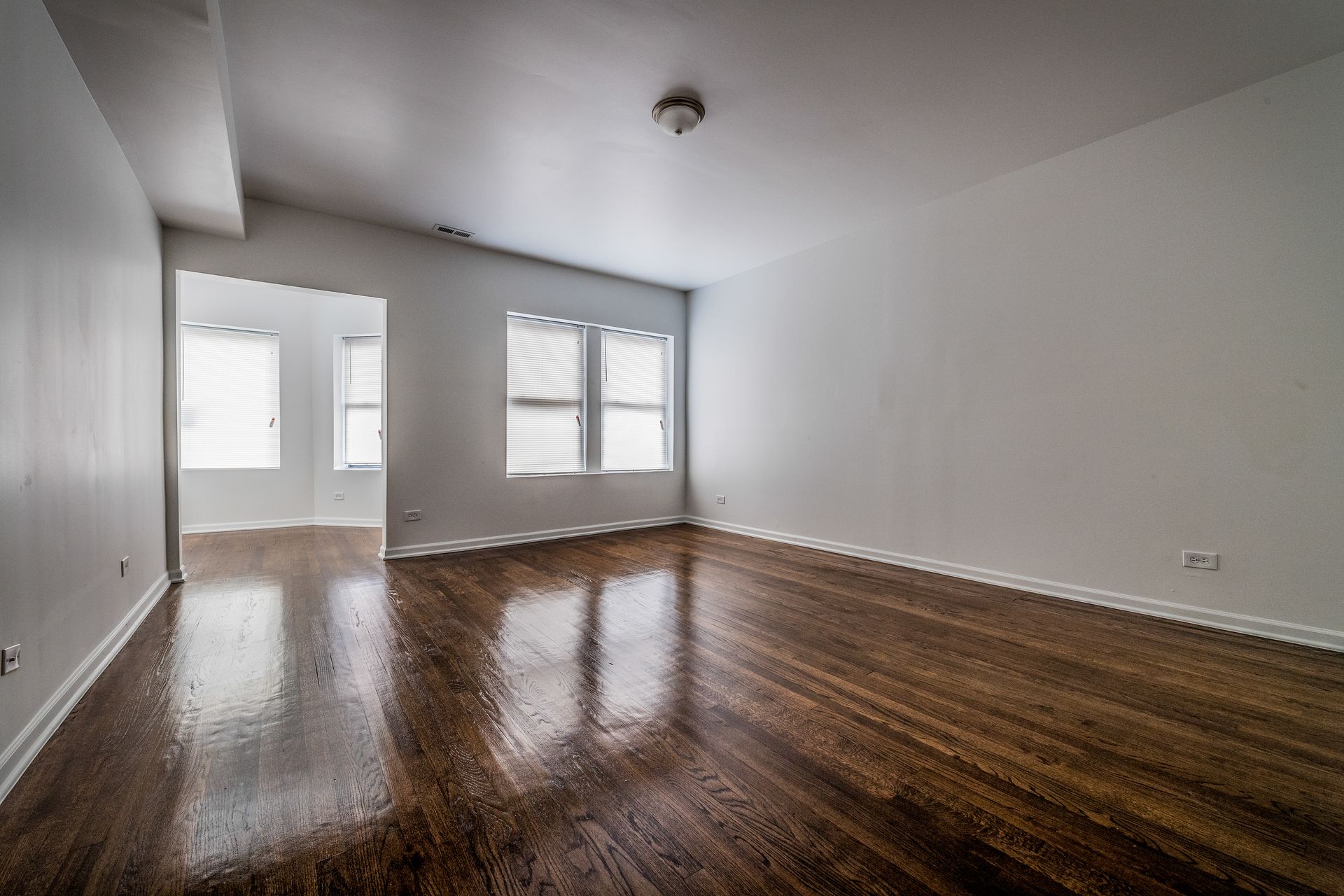 Empty room with dark wood floors, white walls, and two windows with blinds.