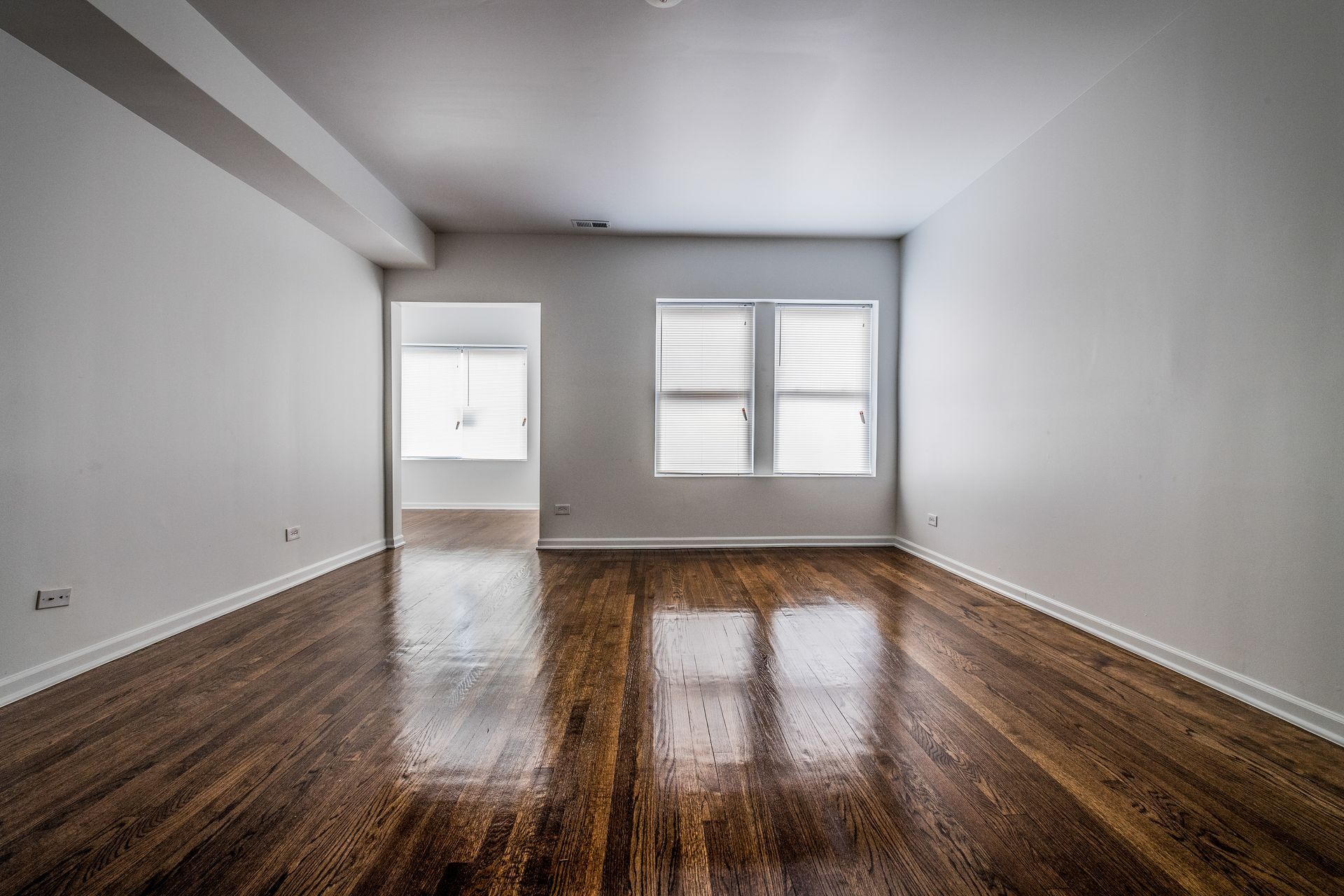 Empty room with wood floors and white walls. Two windows and an open doorway are visible.