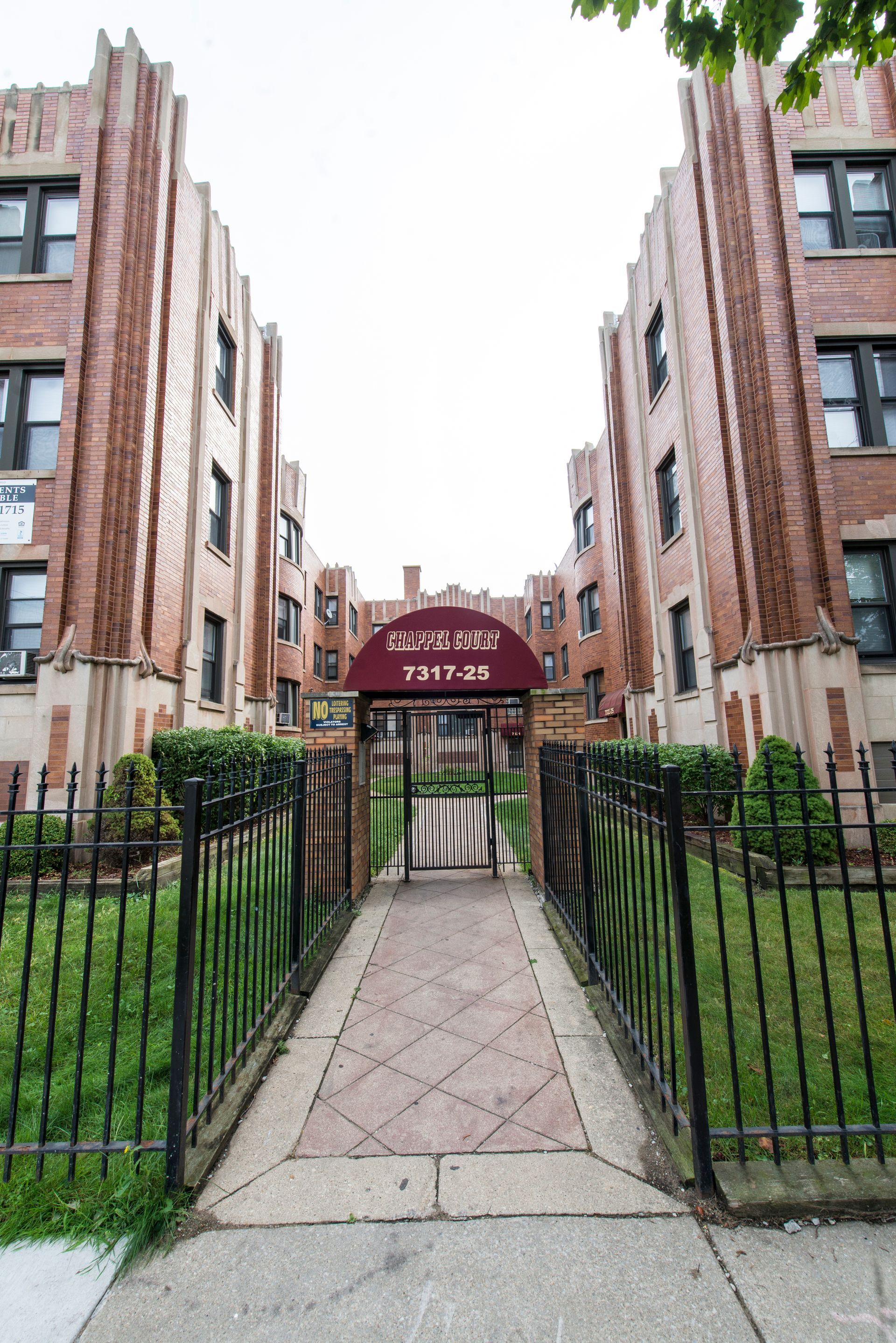 Apartment building with brick facade and arched entrance. A walkway leads to a gated entrance.