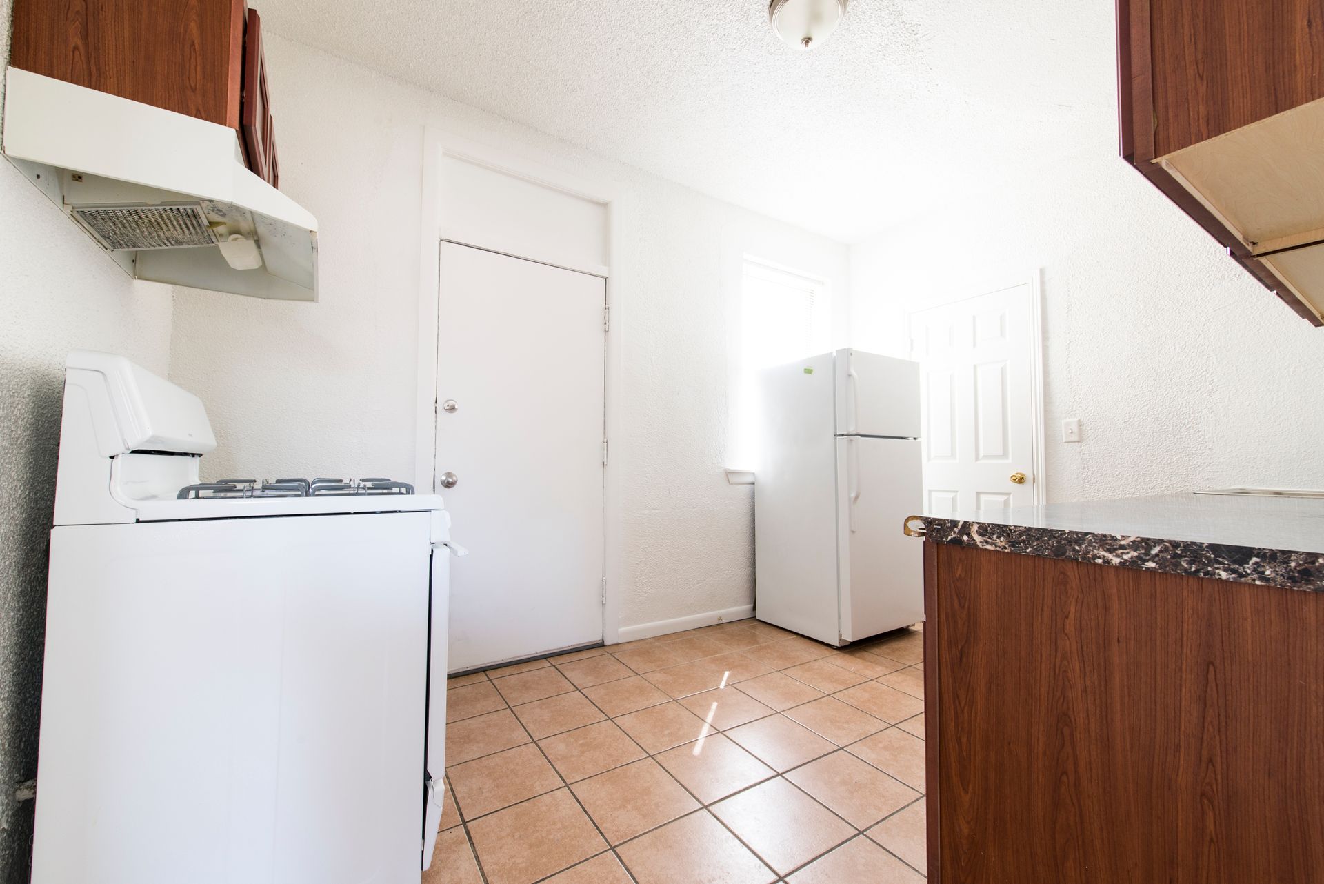 Kitchen with white appliances, brown cabinets, and tan tile floor.