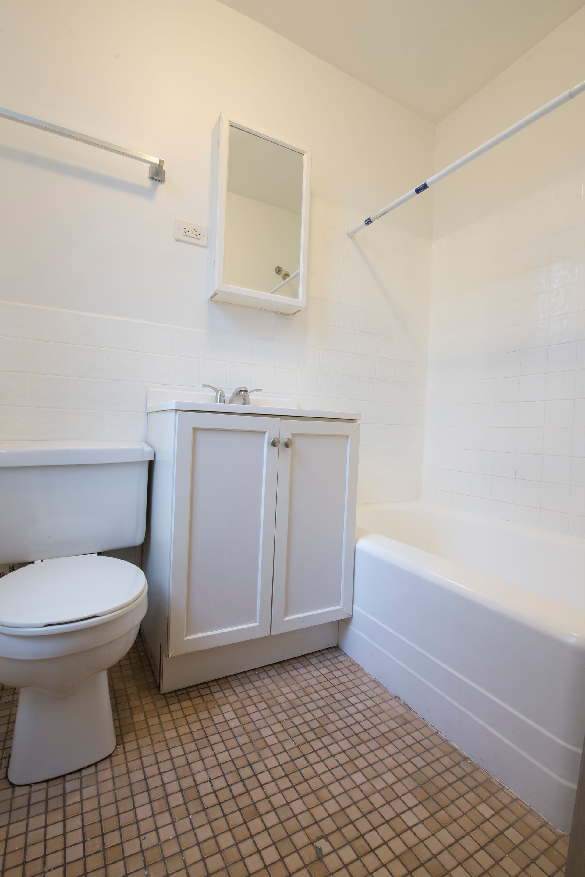 Bathroom with toilet, sink, mirror, and bathtub. White fixtures, tiled floor.