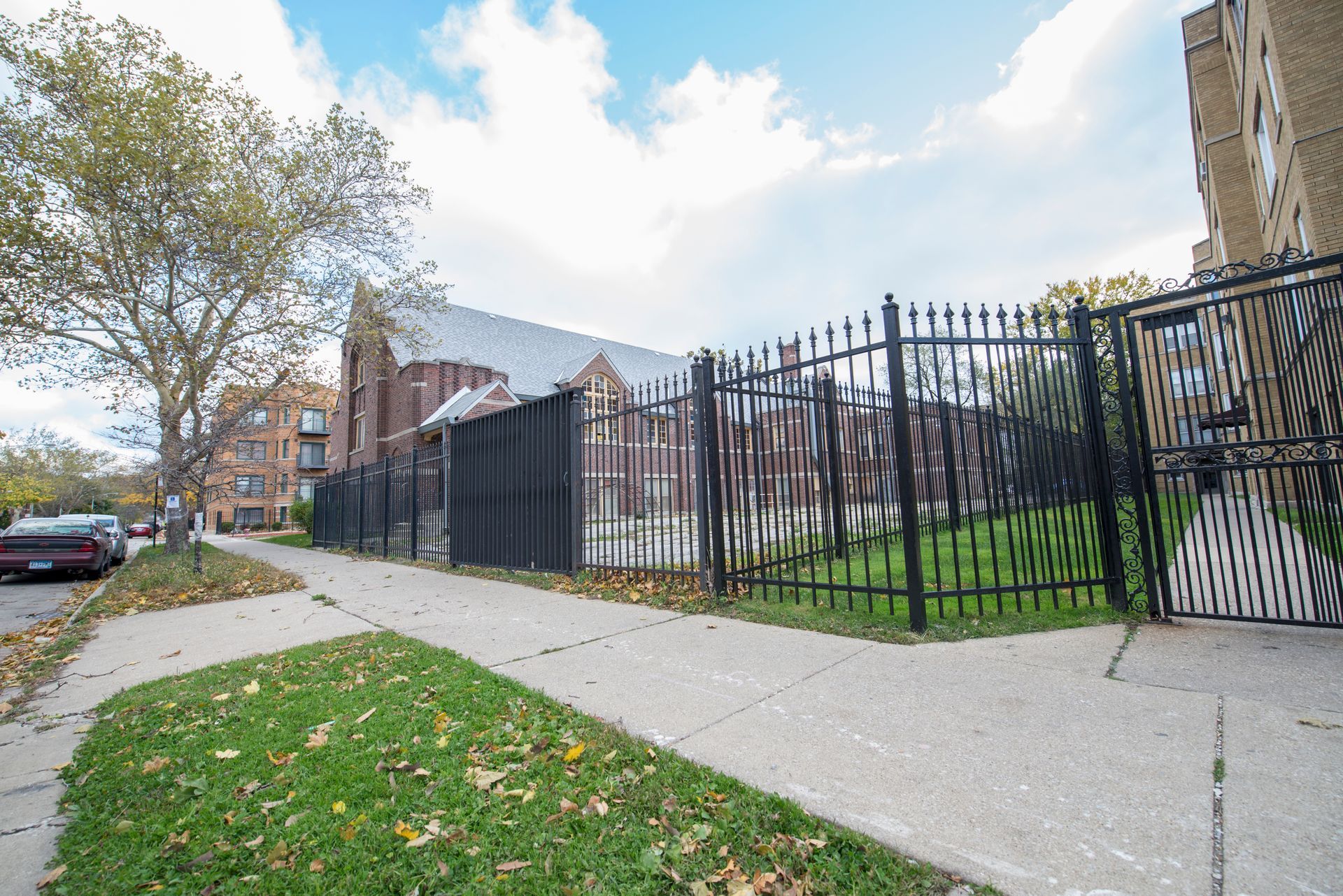 Sidewalk with grass and fence, leading to brick building under cloudy sky.