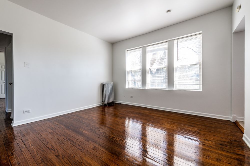 Empty room with hardwood floors, white walls, and a triple window.
