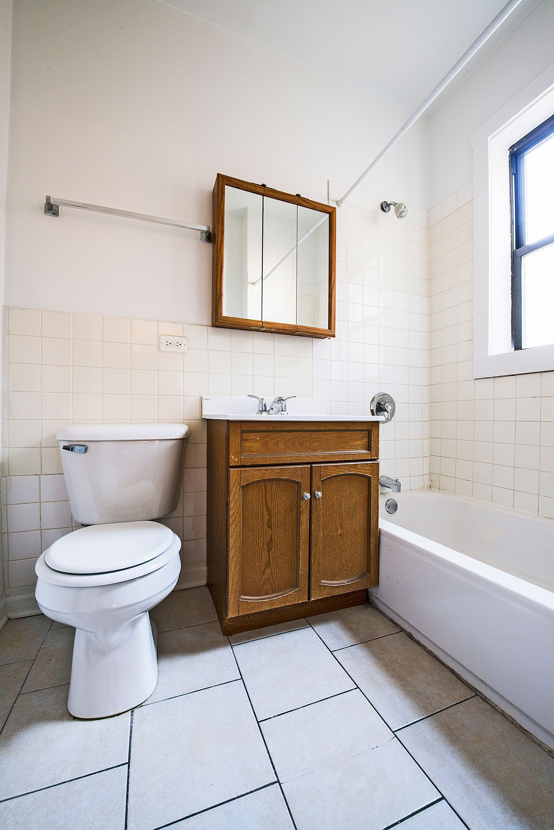 Bathroom with a white toilet, vanity, tub, and window; white tile floor and walls.