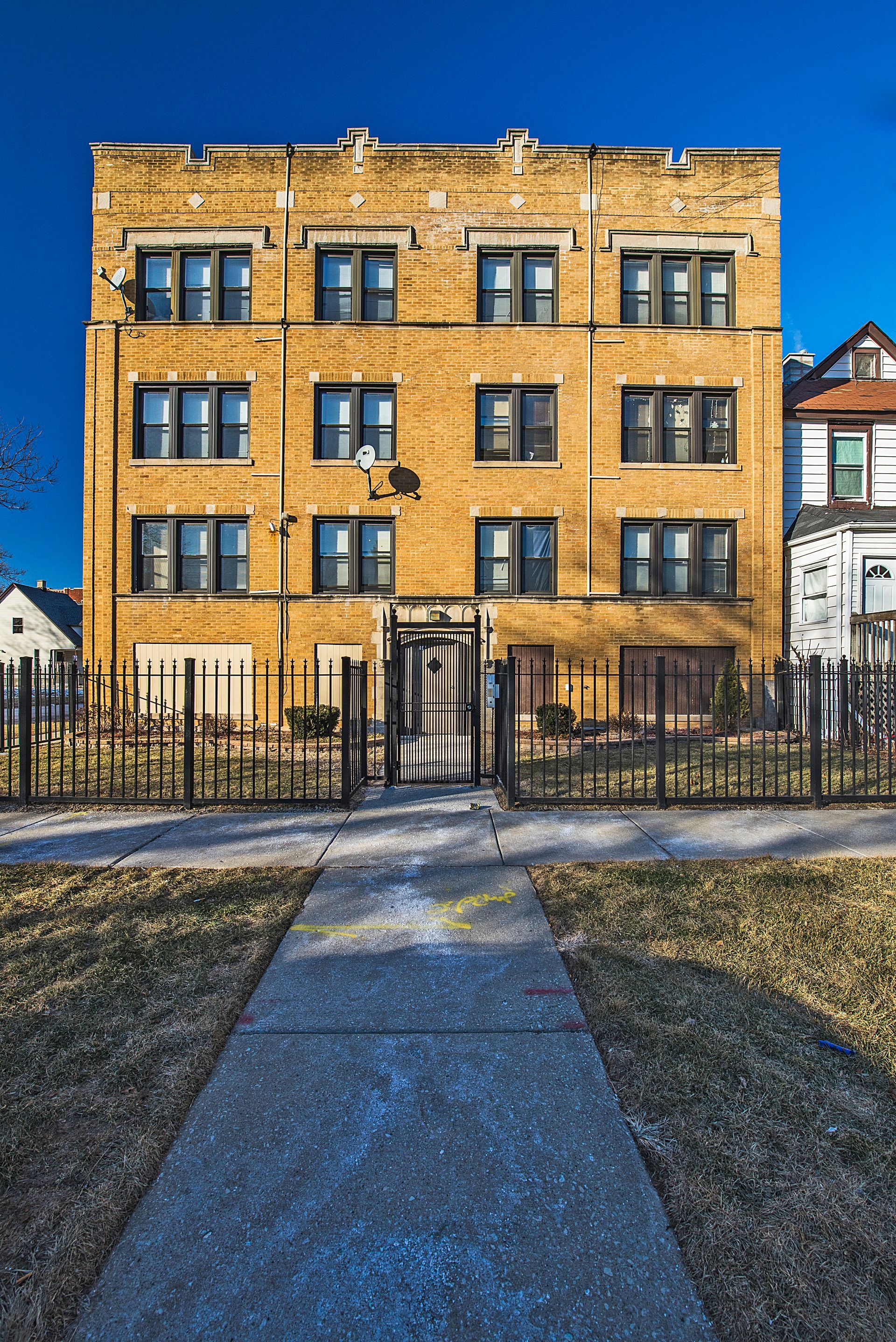 Yellow brick apartment building with dark windows and a black iron fence.
