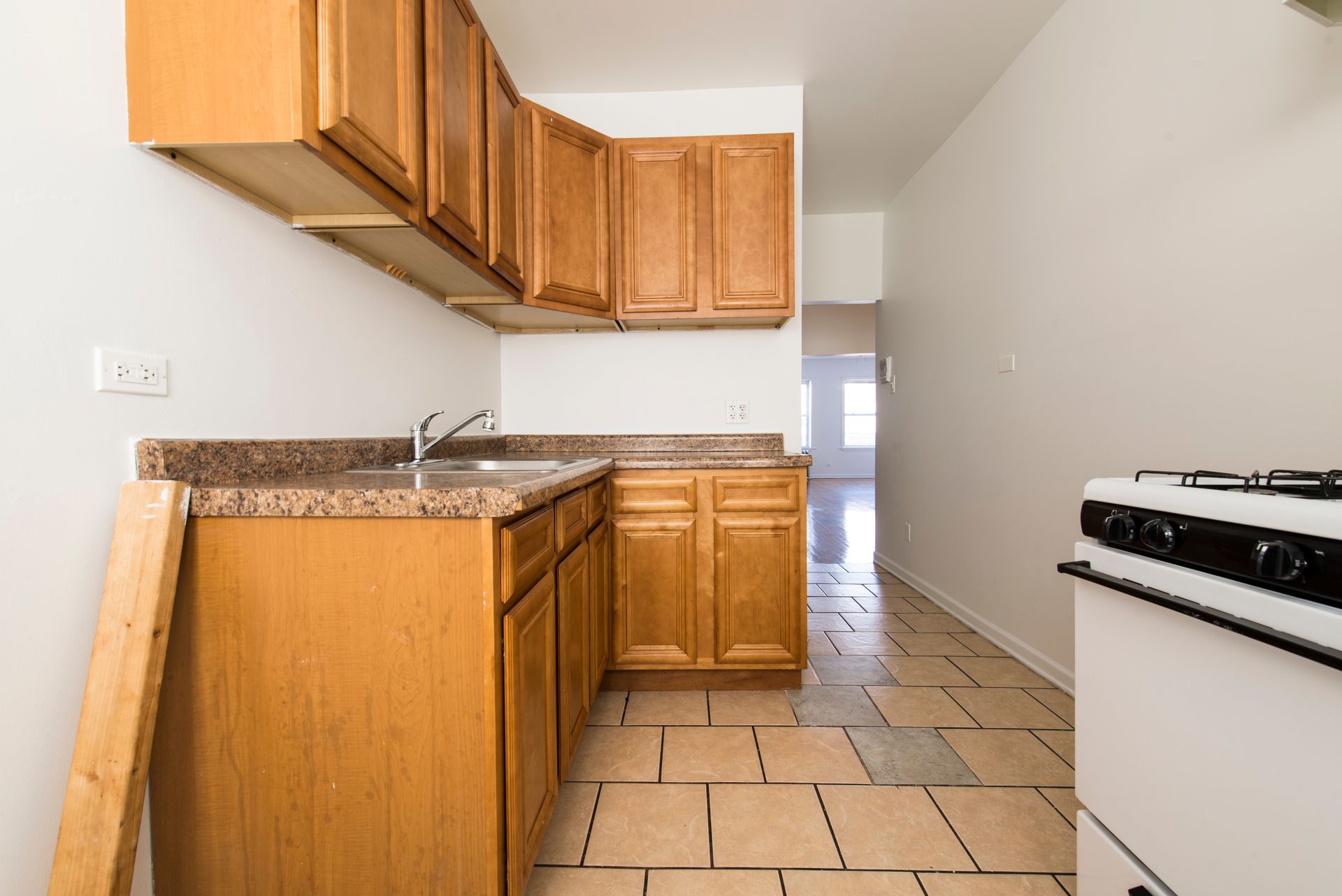 Small kitchen with light brown cabinets, a sink, and a white stove, likely under renovation.
