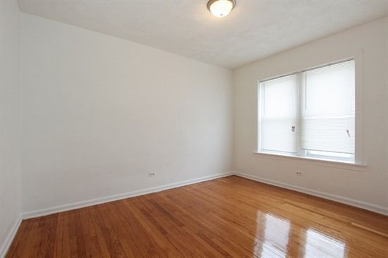 Empty room with hardwood floors, white walls, two windows with blinds, and a ceiling light.