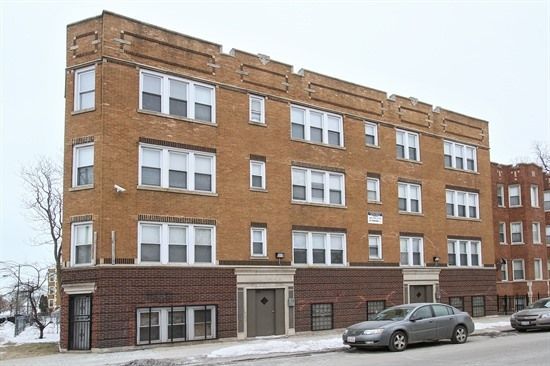 Three-story brick apartment building on a snowy street, car parked in front.