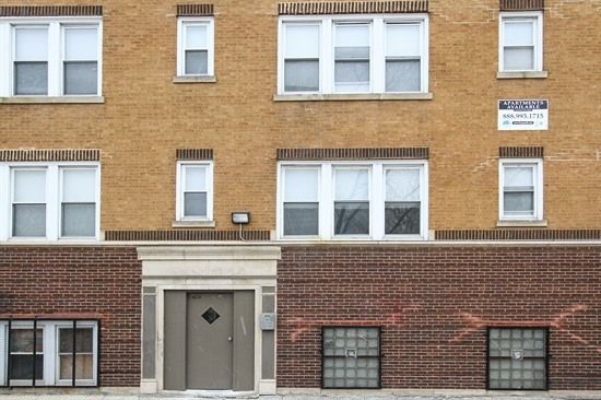 Brick apartment building with white-framed windows, dark brown door, and small sign.