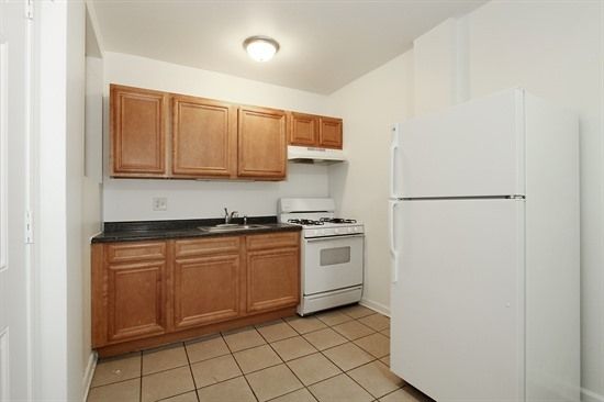 Small kitchen with wood cabinets, white appliances, and tan tile floor.