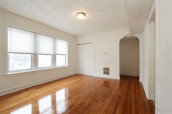 Empty room with hardwood floors, large windows, and a doorway.