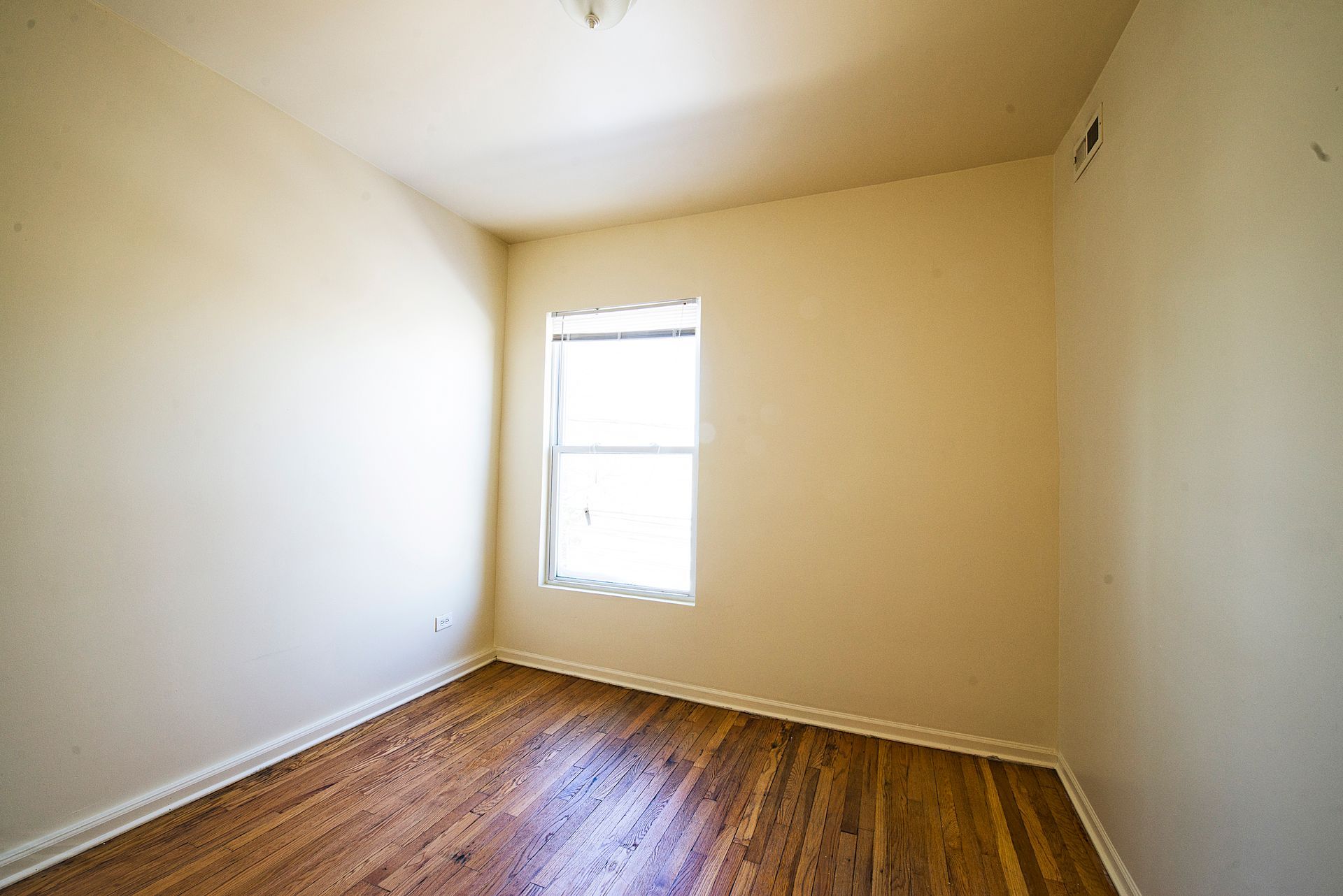 Empty room with hardwood floors, a small window, and light-colored walls.