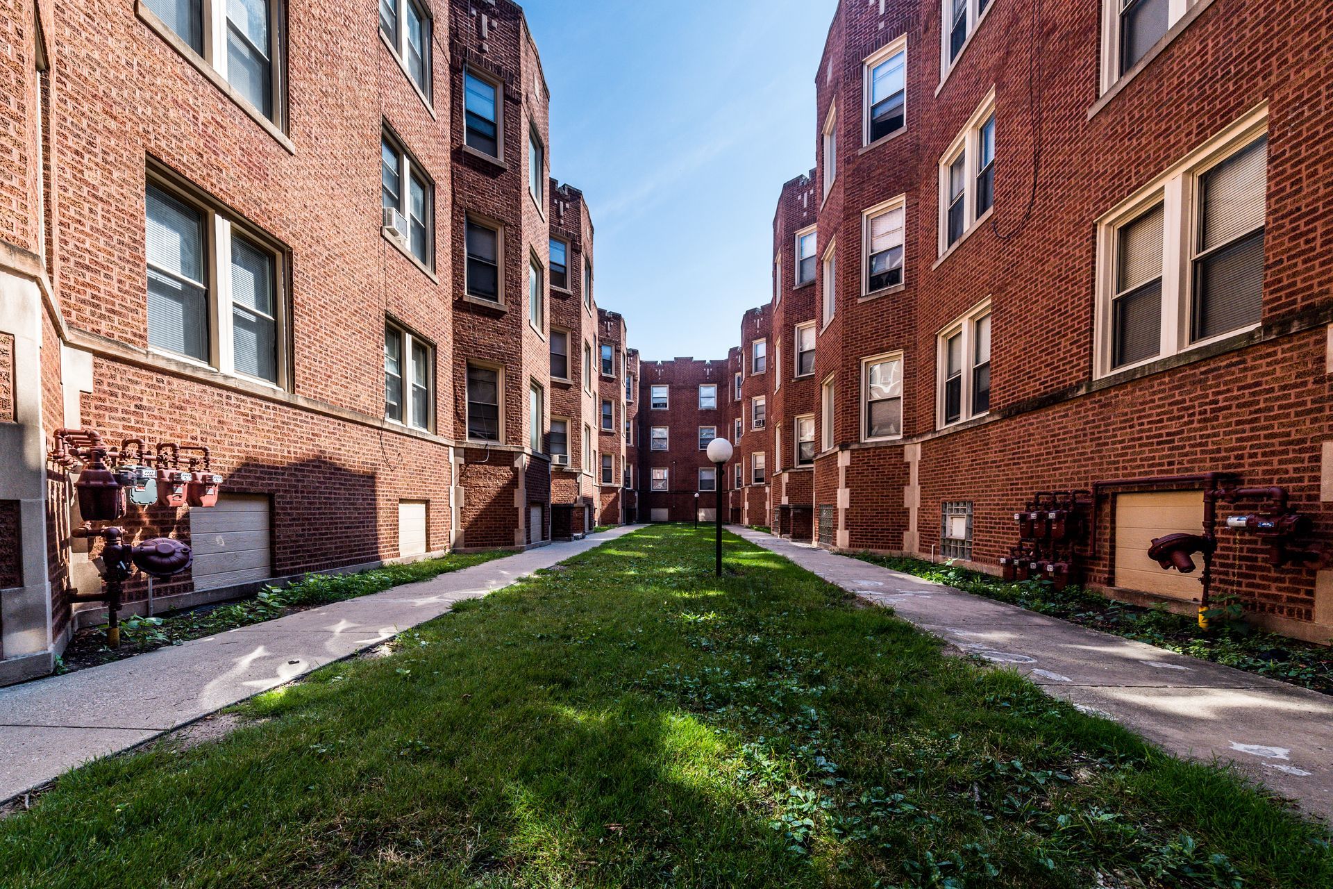Brick apartment buildings flank a grassy walkway on a sunny day.