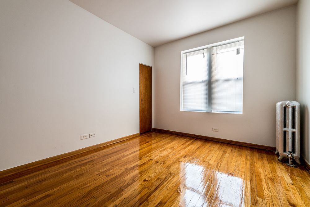 Empty room with hardwood floors, white walls, a window with blinds, and a radiator.