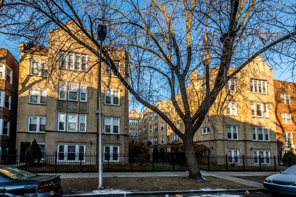 Apartment buildings with beige facades on a sunny day; leafless tree in foreground.