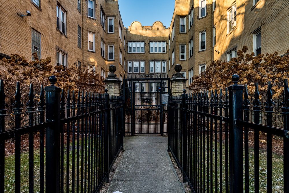 Gated courtyard entrance between two multi-story brick apartment buildings, sunlight.