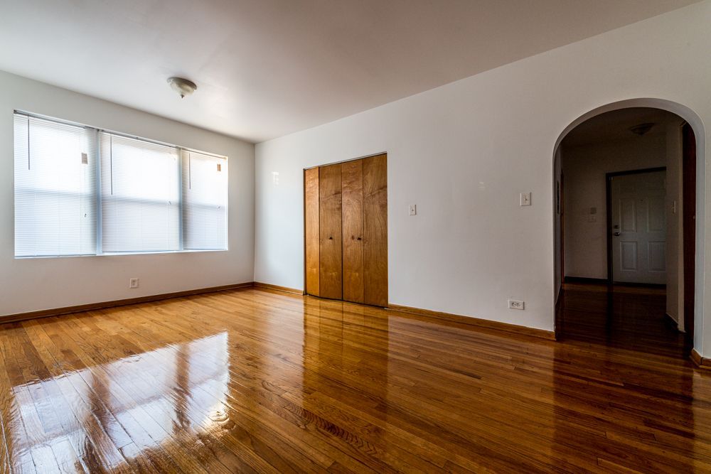 Empty room with hardwood floors, a window, closet doors, and an arched doorway.