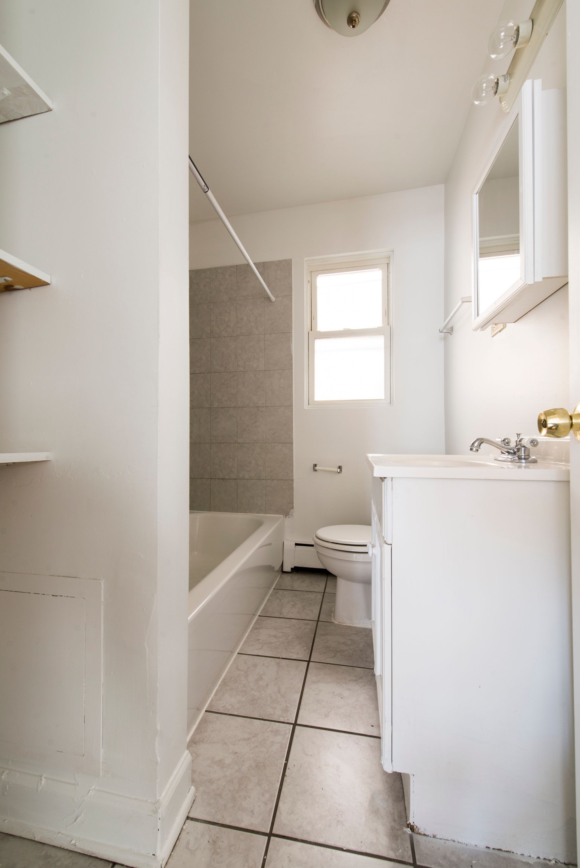 Bathroom with white walls, tub, toilet, and vanity with a window. Tile floor.