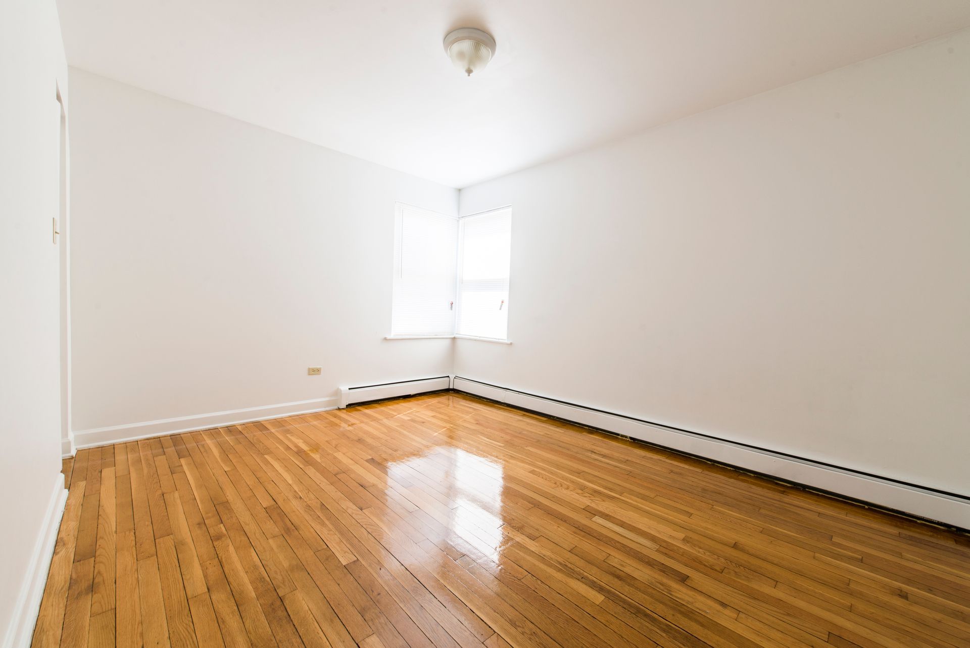 Empty room with hardwood floors, white walls, and a small window in the corner.