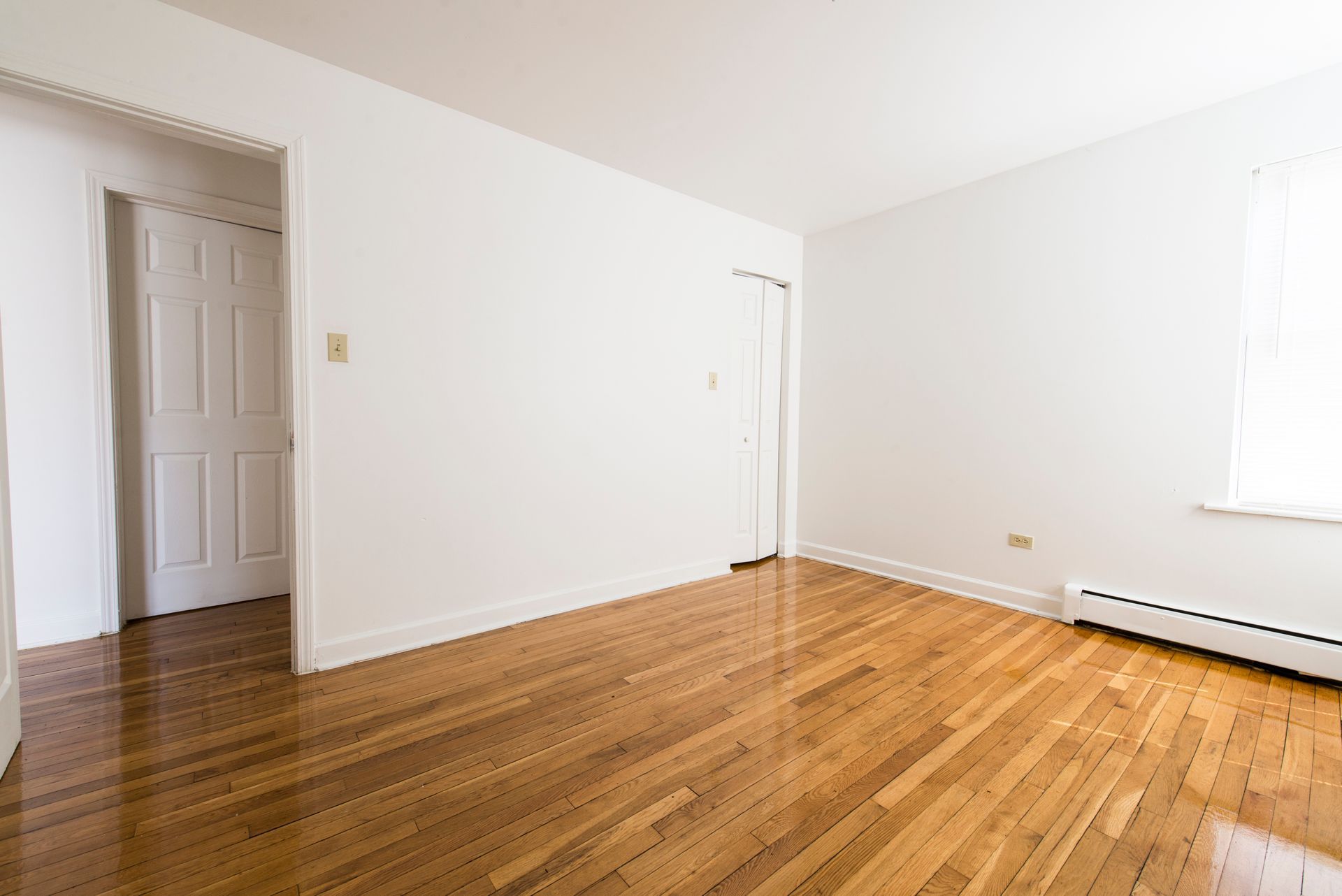 Empty room with hardwood floors, white walls, and closed doors.