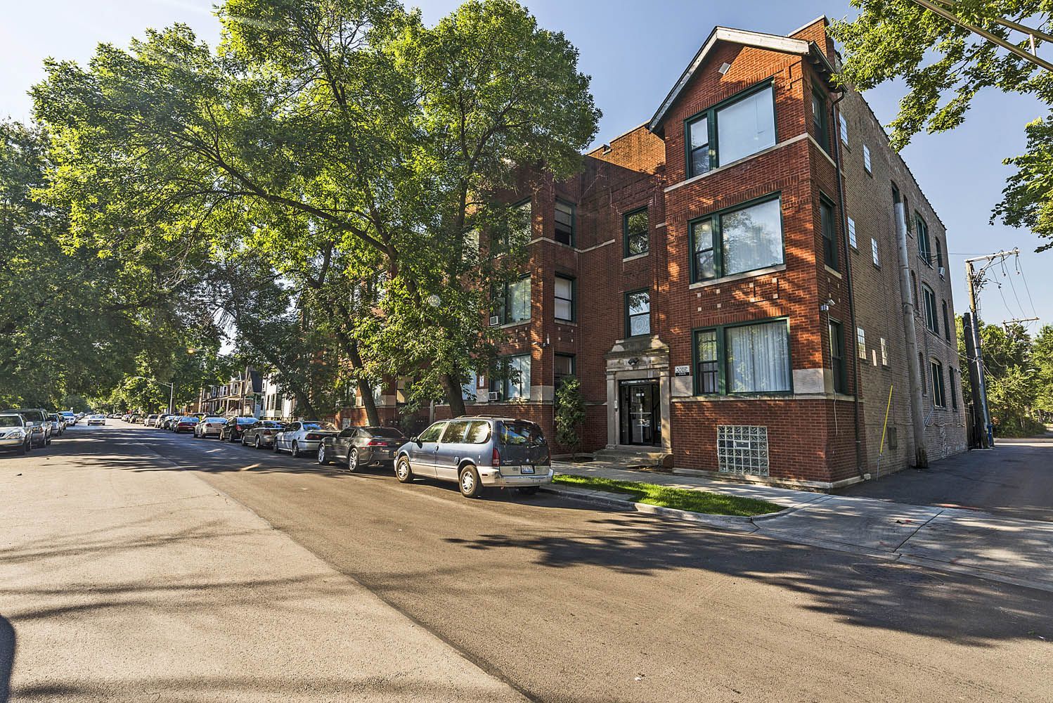 Apartment building on a tree-lined street with cars parked along the side.