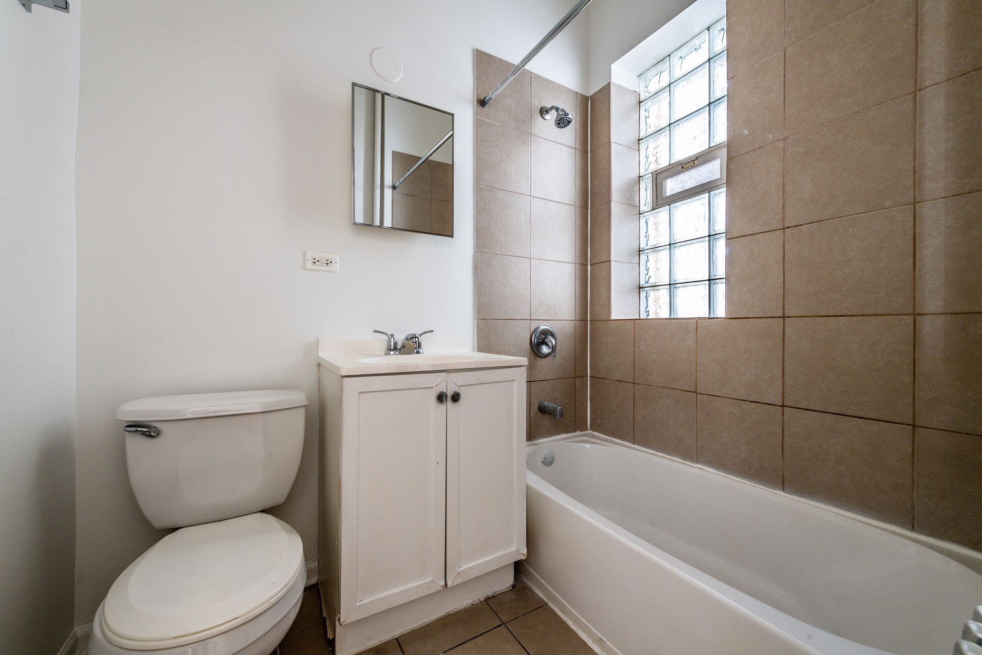 Bathroom with white toilet, vanity, and bathtub. Beige tiled wall and a window.