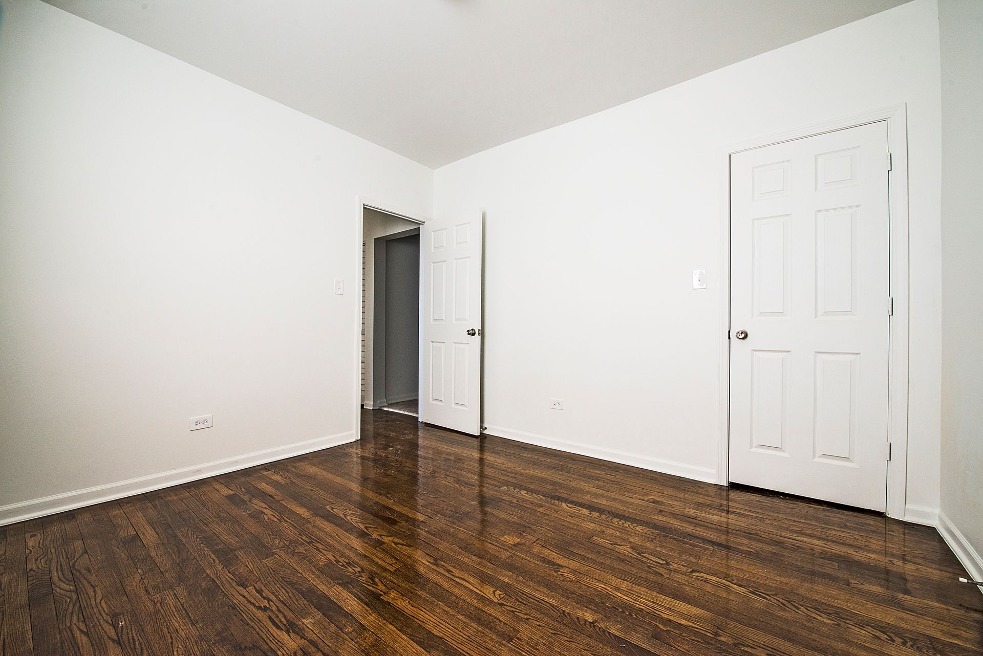 Empty room with dark wood floors, white walls, and two white doors.