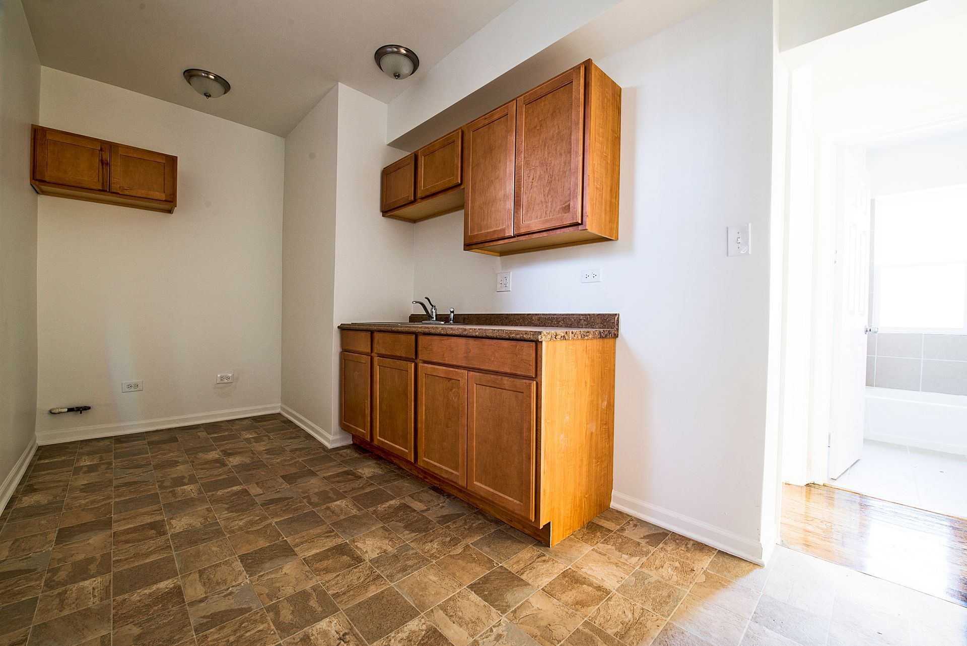 Small kitchen with brown cabinets and countertop, sink, and open doorway to another room.